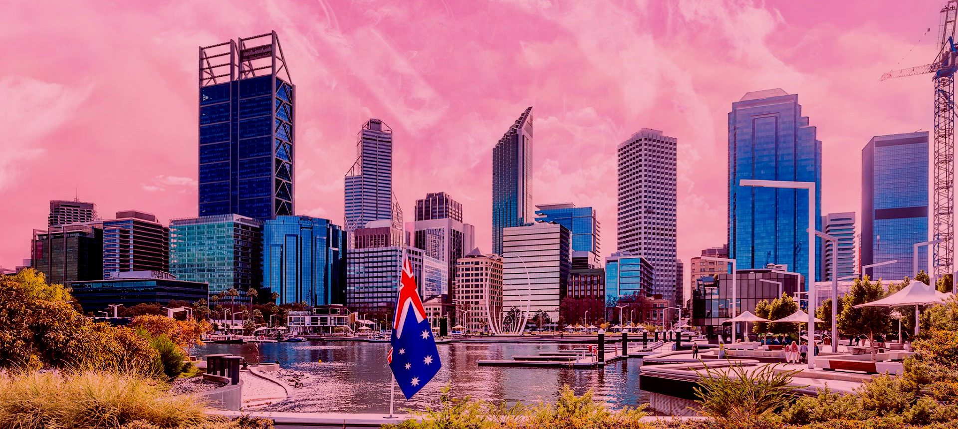Panorama con grattacieli sul lungomare, bandiera australiana in primo piano e cielo dalle tonalità rosa.